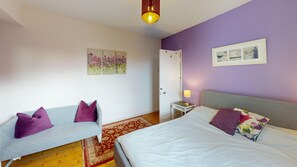 A bedroom with a bed, a sofa, a nightstand, a lamp, and artwork on the walls. - Mill House | Oxford Holiday Let | 2 Beds & Sleeps 4 (Oxford)