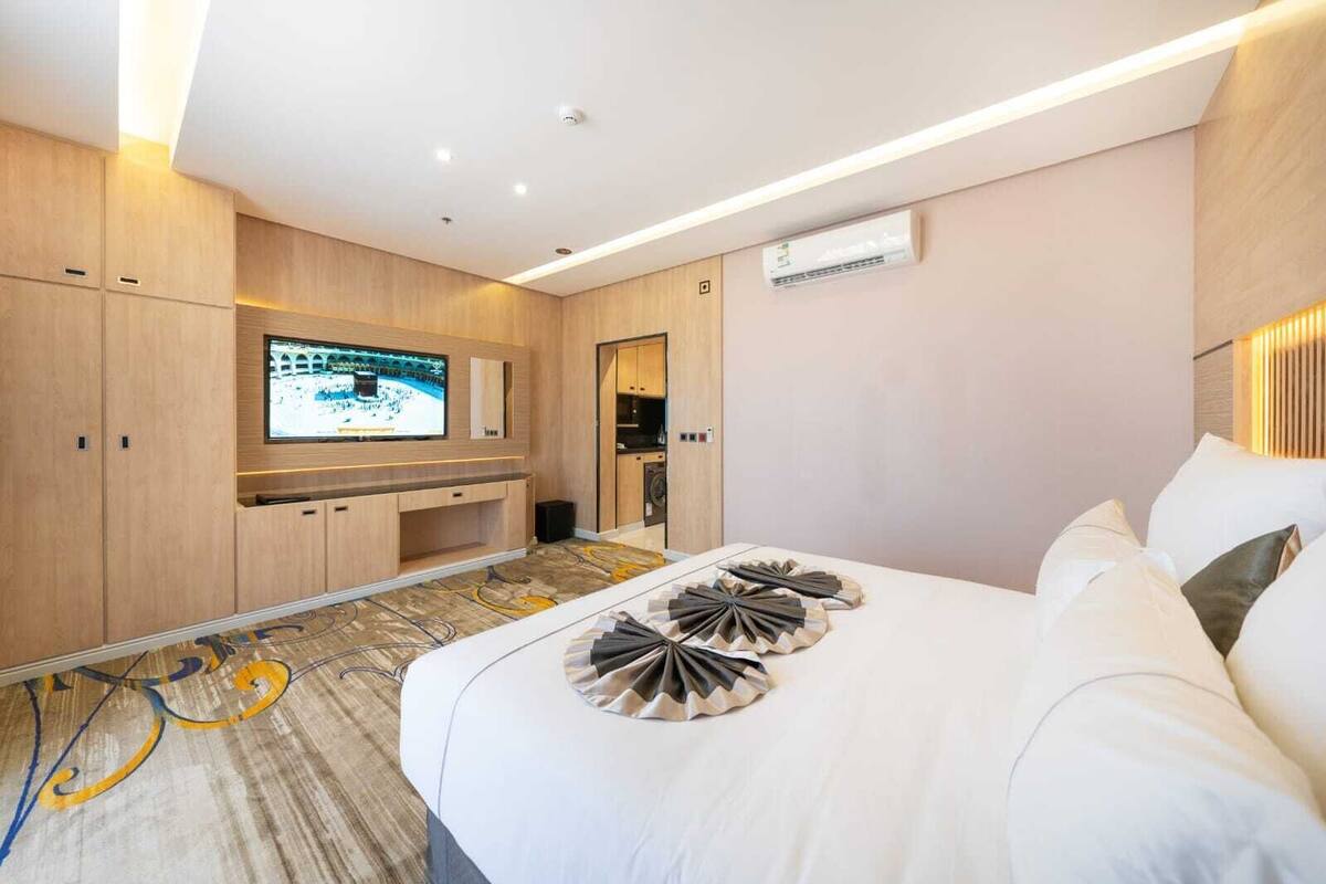 Una habitación de hotel moderna con una cama grande, un televisor de pantalla plana en la pared, un armario empotrado y una pequeña cocina.
