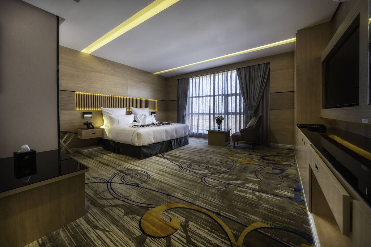 Una habitación de hotel moderna con una cama grande, televisión, escritorio y ventana con cortinas.