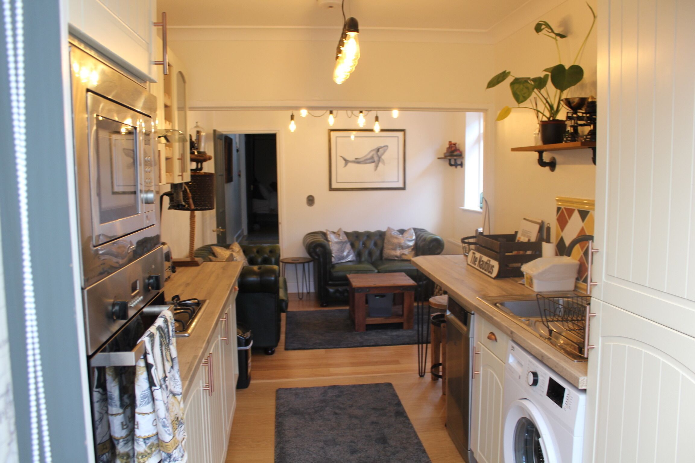 Una cocina compacta con lavadora, una zona de comedor con sofá y una mesita pequeña.