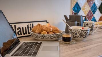 Um laptop, um prato de croissants, uma chávena de café e uma chaleira sobre uma mesa.