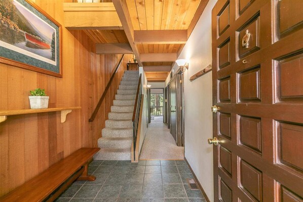 A wooden interior hallway with a staircase, a bench, and a door.