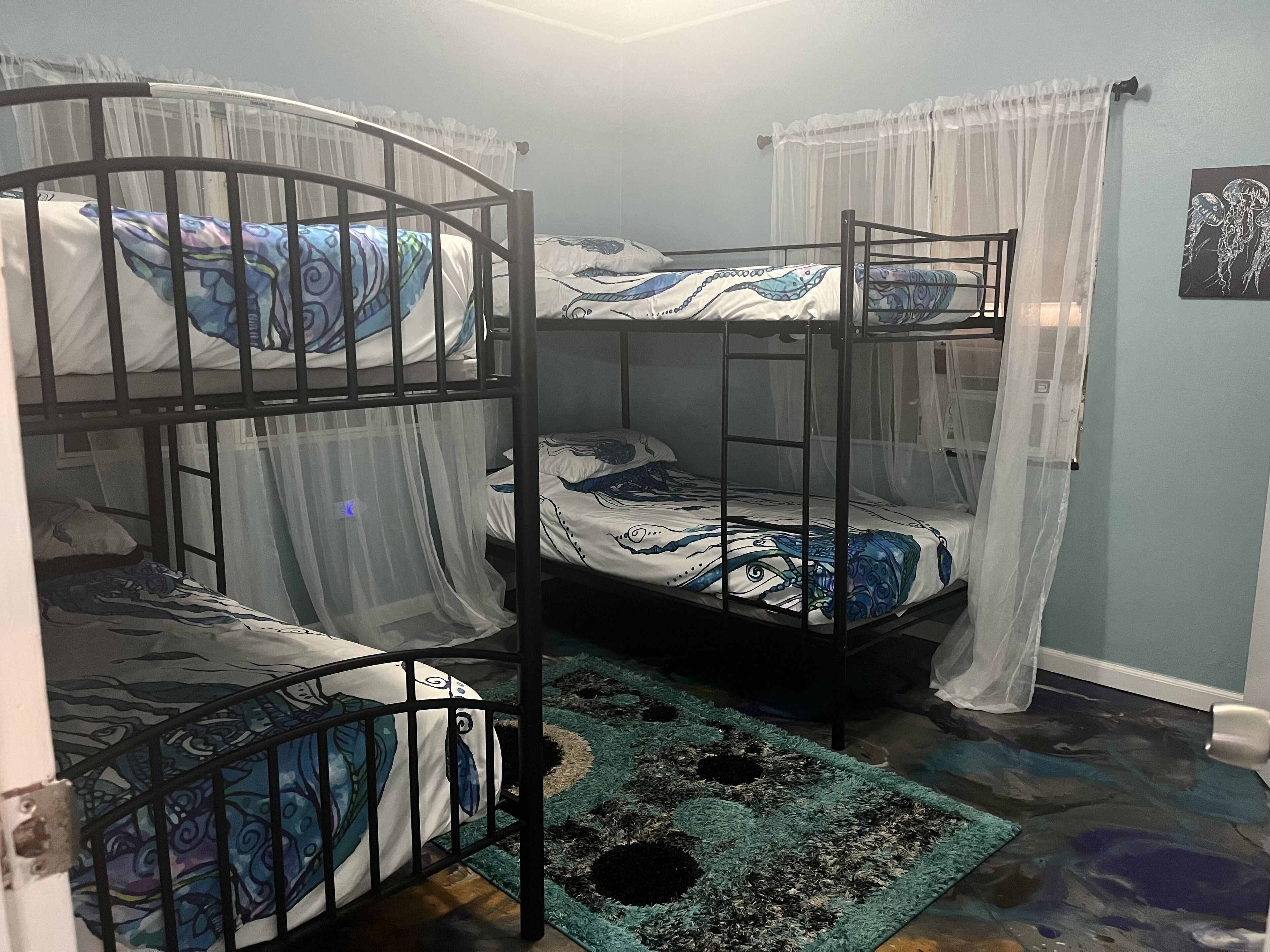 A bunk bed room with two beds, each with a canopy. The room has a blue wall and a patterned rug on the floor.