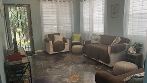 A living room with a dark, colorful floor, a brown sofa, a beige armchair, and a small table with a plant. - Peaceful, fully renovated home that is solar powered!   (Rincon)