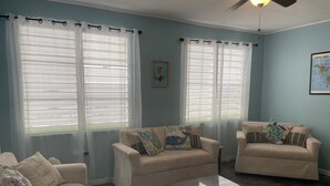 A living room with two beige sofas, a glass coffee table, and sheer curtains on the windows. - Peaceful, fully renovated home that is solar powered!   (Rincon)