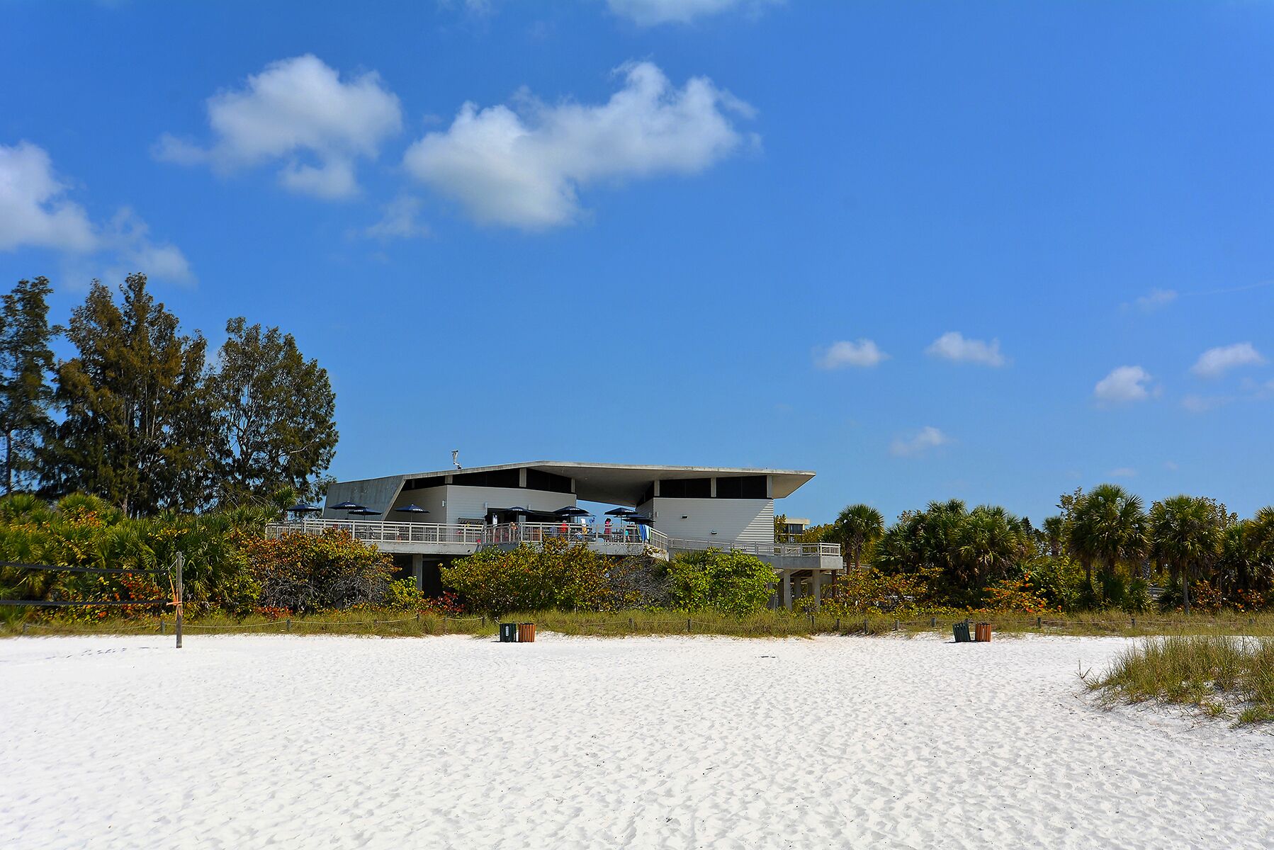 A modern building with a flat roof and multiple levels, surrounded by a sandy beach and dense greenery.