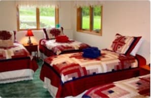 Une chambre à coucher avec deux lits simples, chacun recouvert d’une couette rouge et blanche, une table de chevet avec une lampe, et une fenêtre donnant sur un paysage verdoyant.