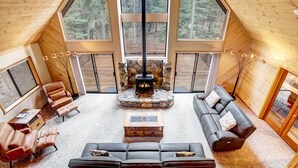 Ein gemütlicher Innenraum mit einem Kamin aus Stein, Ledersofas und großen Fenstern mit Blick auf einen Wald.
