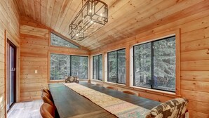 Ein Holzinterieur mit einem langen Esstisch, großen Fenstern und einer Chandelier.