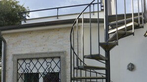 Eine Wendeltreppe führt zu einer zweiten Etage, ein Fenster mit schmiedeeisernen Gitterstäben und eine Außenwand aus Backstein.