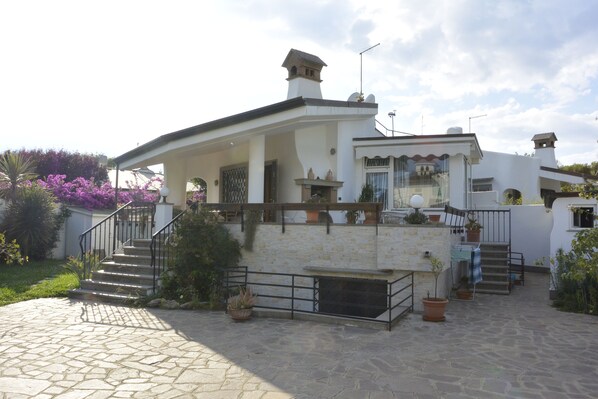 A two-story house with a stone staircase, a covered porch, and potted plants. - villa with garden 100 meters from the sea (Fiumicino)