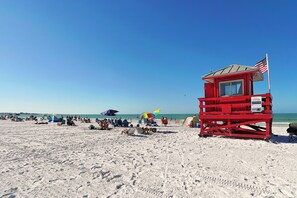 Ein Strand mit einem Rettungsturm, Sonnenschirmen und entspannten Menschen.