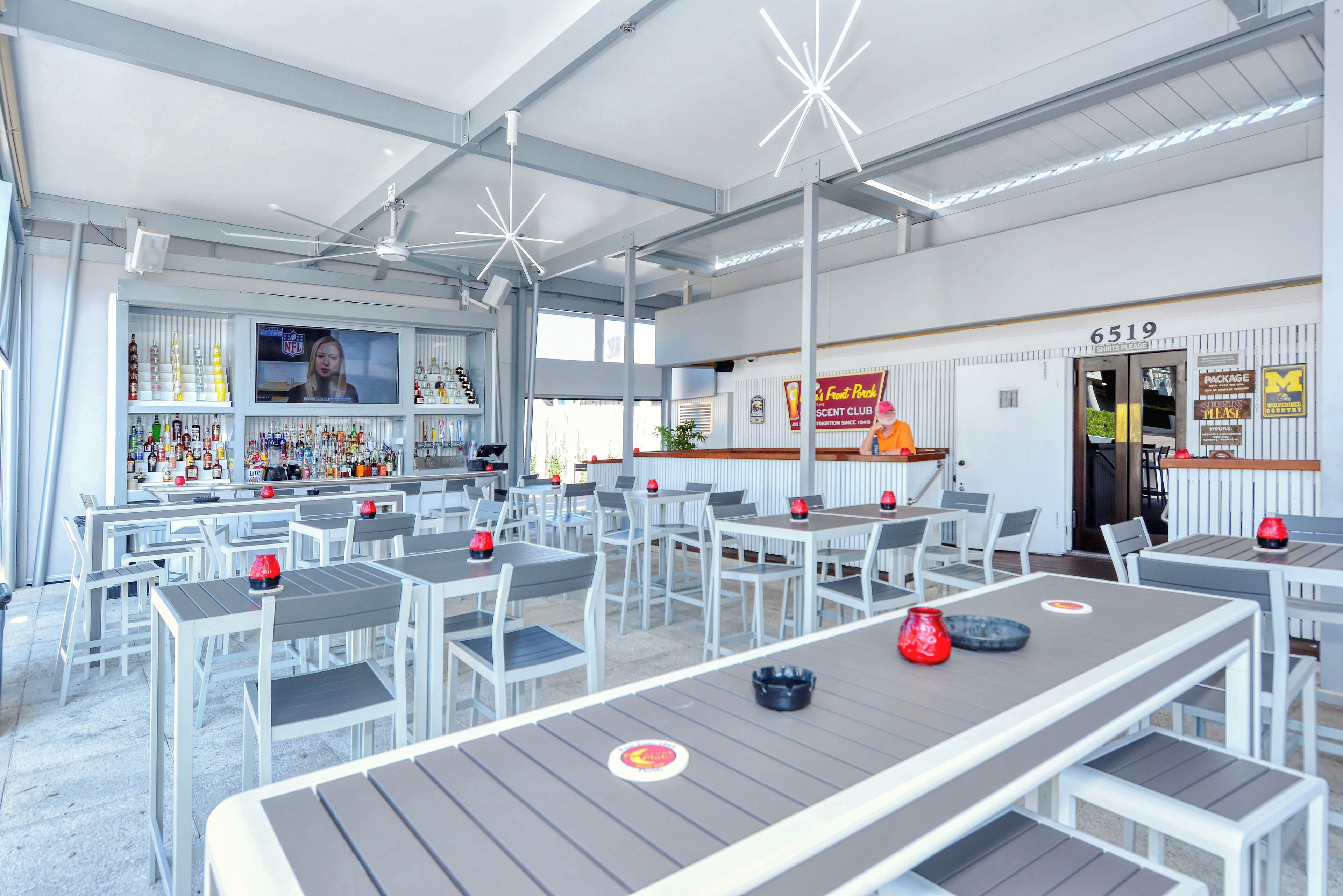 A spacious indoor area with multiple tables and chairs, a bar area with a television displaying the NFL, and a sign indicating the address 6519.