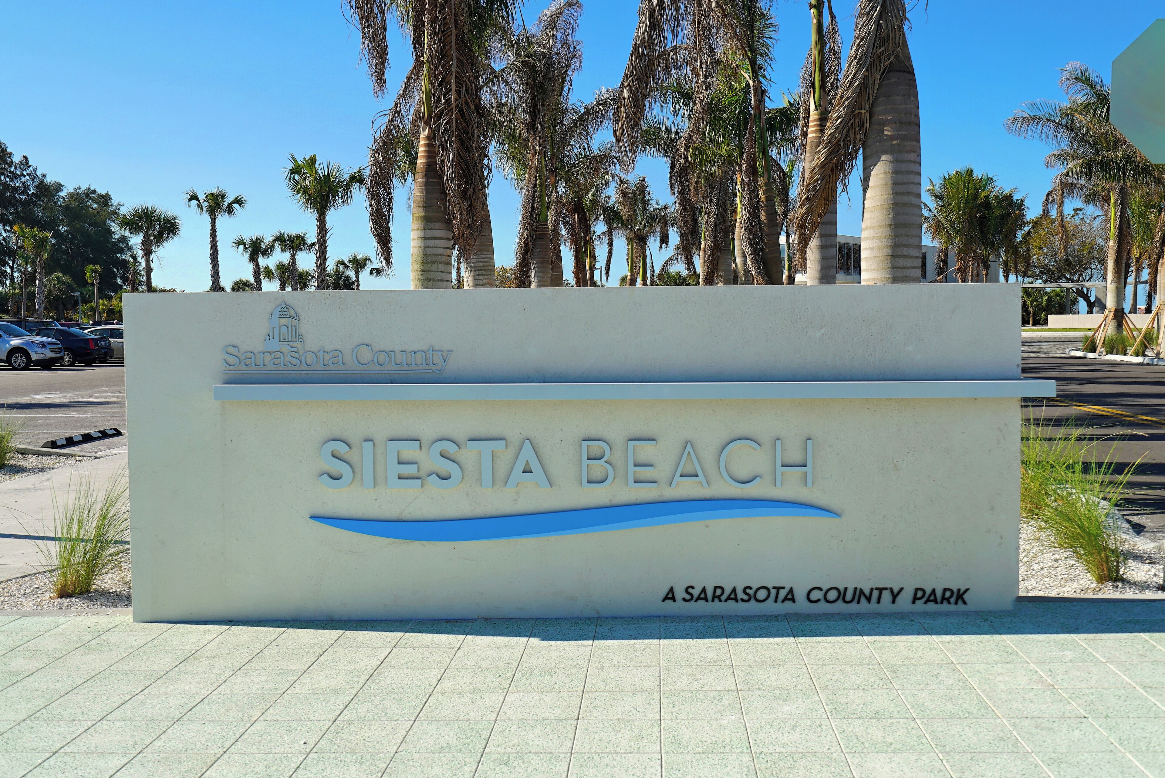 A sign for Siesta Beach, a Sarasota County park, with palm trees in the background.