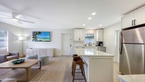 Una cocina moderna con armarios blancos, un refrigerador de acero inoxidable y un comedor con una mesa de madera y taburetes de bar.