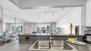 Una cocina moderna con encimeras de granito, un lavamanos doble y vista al área de estar con un balcón.
