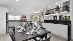Una cocina moderna con comedor, con una mesa larga dispuesta para una comida, un balcón con barandilla y vistas al exterior.