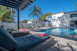 Ein moderner Poolbereich im Freien mit Liegestuhl, Tisch am Pool und einer Pergola.
