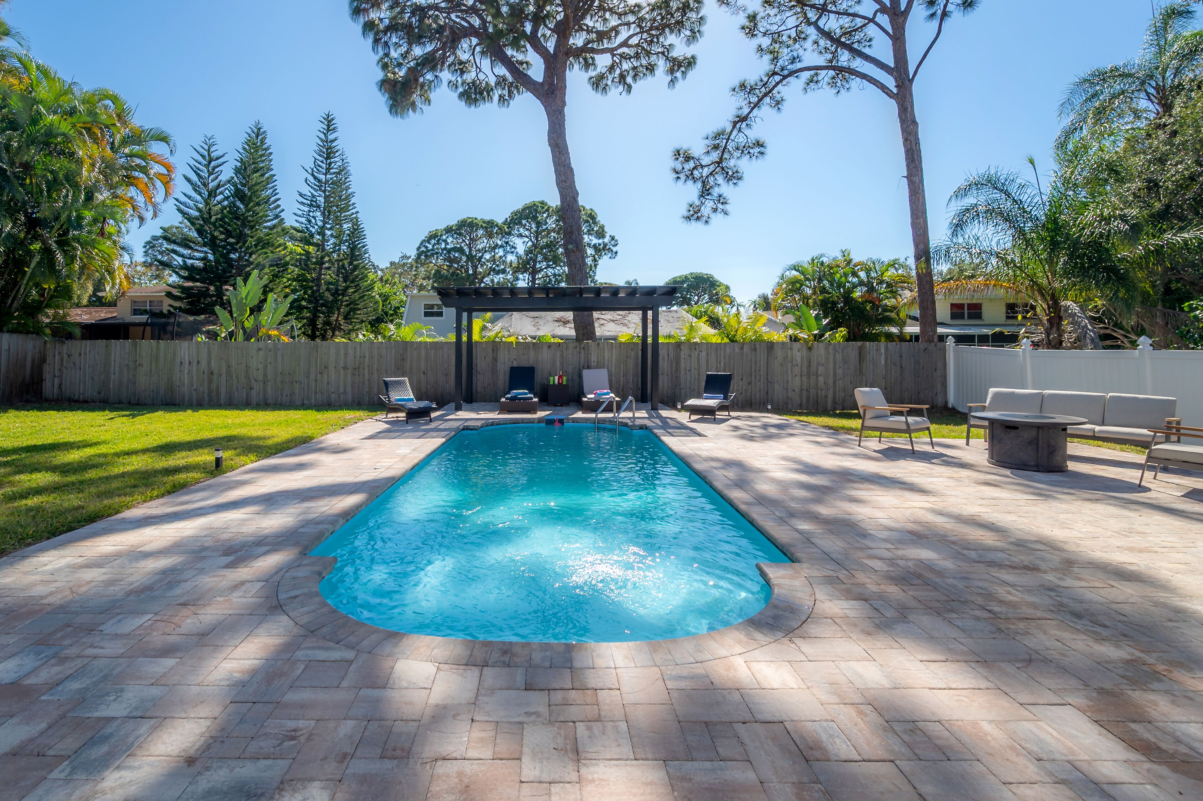 Una piscina rectangular con una pérgola y sillas de descanso en un patio trasero.
