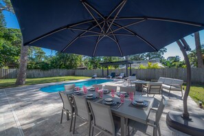 Eine Außenpatio mit Pool, Esstisch für vier Personen und einem großen Sonnenschirm.