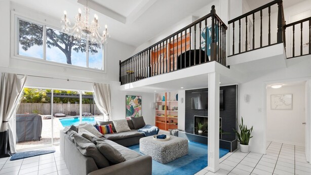 Amplia sala de estar con un sofá modular grande, un tapete azul, una chimenea y un balcón con piscina.