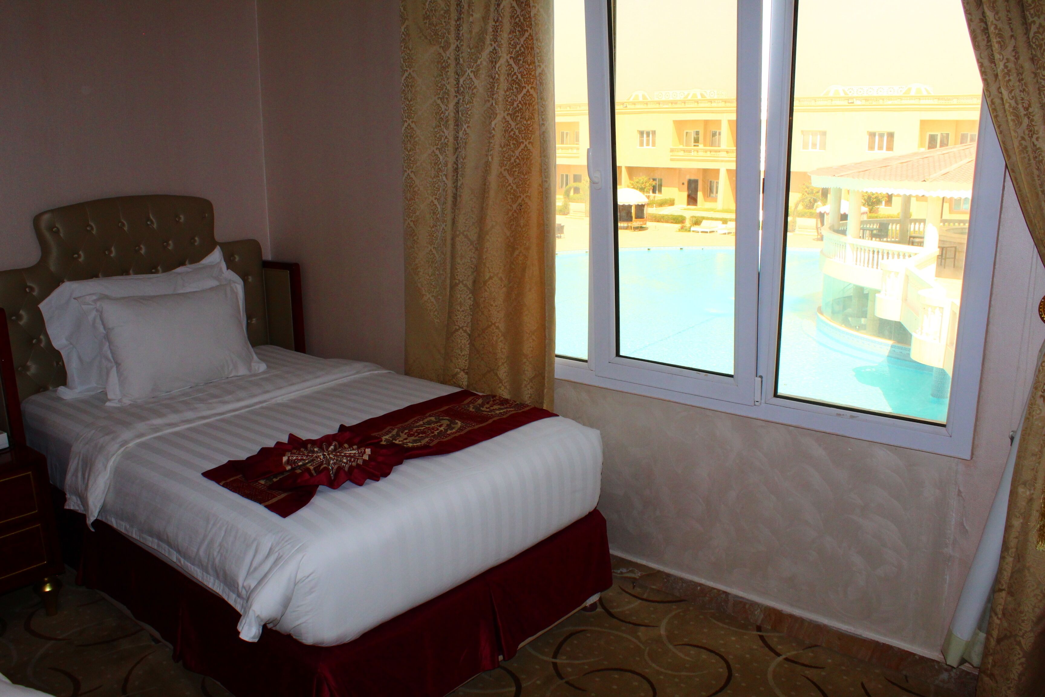 A hotel room with a large bed, a window with curtains, and a view of a pool and building.