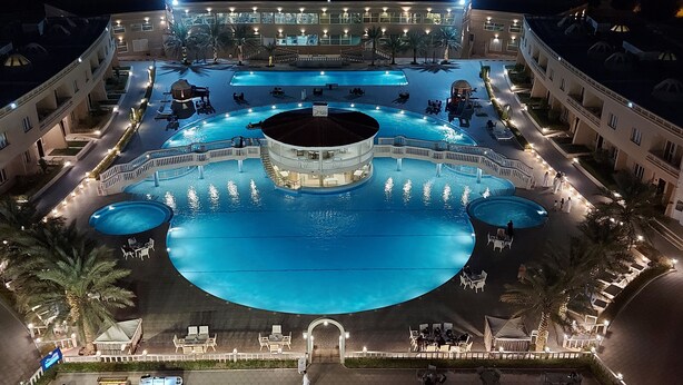 A large, multi-level swimming pool complex with multiple pools and sunbathing areas, surrounded by buildings with outdoor seating and lighting. - Al Salam Grand Hotel & Resort (Al Buraymi)