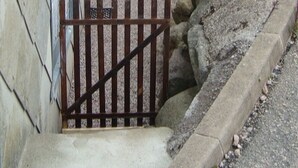 Eine Steinsäule mit einem Metallgitter, das zu einem bepflasterten Bereich führt.
