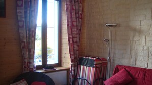 Ein gemütliches Zimmer mit einem roten Sofa, einem Korbsessel und einer Streifen-Tasche.