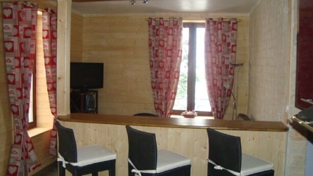 Ein Raum mit Holzwänden, einer Bar, zwei Barhocker, einem Fernseher und gemusterten Vorhängen.
