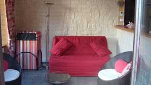 Ein gemütlicher Wohnbereich mit einem roten Sofa, zwei Korbstühlen, einem kleinen runden Tisch und einem gestreiften Sessel.