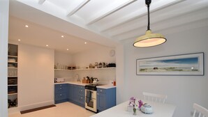 Een moderne keuken met blauwe kastjes, een wit aanrechtblad en een eethoek met een witte tafel en stoelen.
