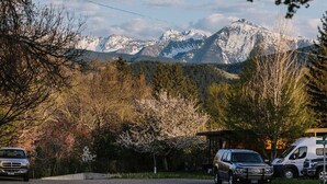 Un estacionamiento con montañas al fondo, un pabellón y una autocaravana.