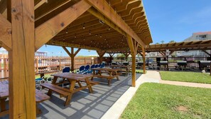 An outdoor wooden pavilion with picnic tables and chairs, surrounded by a wooden fence and a grassy area.