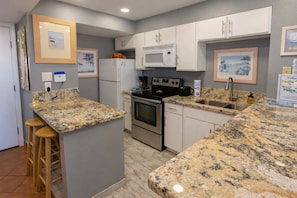A kitchen with granite countertops, a stove, a microwave, and a refrigerator.