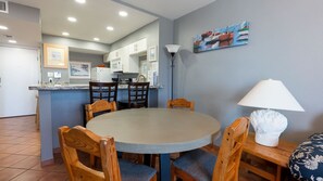 A dining area with a round table, wooden chairs, a lamp, and a painting on the wall.