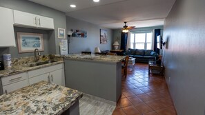 A kitchen with granite countertops, a dining area with a sofa, and a living room with a ceiling fan.