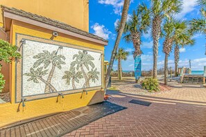 Een gebouw aan het strand met een mozaïek muurschildering, palmbomen en een heldere lucht.