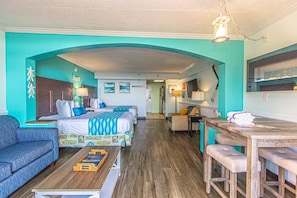 A room with two beds, a sofa, a dining table, and a kitchen area.