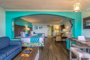 Una habitación de hotel con una cama grande, un sofá, una mesita y una kitchenette.