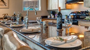 A well-lit kitchen with a granite countertop, a wine bottle, and neatly set dining table with plates, glasses, and a napkin. - Park City Ski Trip - Lift Line Condo Hot Tub (Park City)