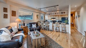 A modern living room with a leather sofa, a wooden coffee table, and a kitchen area with a bar and stools. - Park City Ski Trip - Lift Line Condo Hot Tub (Park City)
