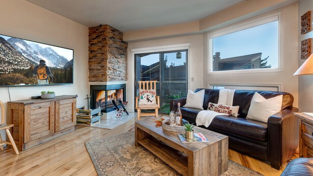 A cozy living room with a fireplace, a large TV, a leather sofa, and a wooden coffee table. - Park City Ski Trip - Lift Line Condo Hot Tub (Park City)