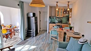 Une cuisine compacte dotée d’appareils électroménagers modernes, un coin repas avec une table et des chaises, et un coin salon confortable avec un canapé et un chapeau posé sur les coussins.