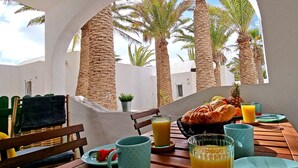 Une table dressée pour le petit-déjeuner, avec des chaises et une vue sur des palmiers.