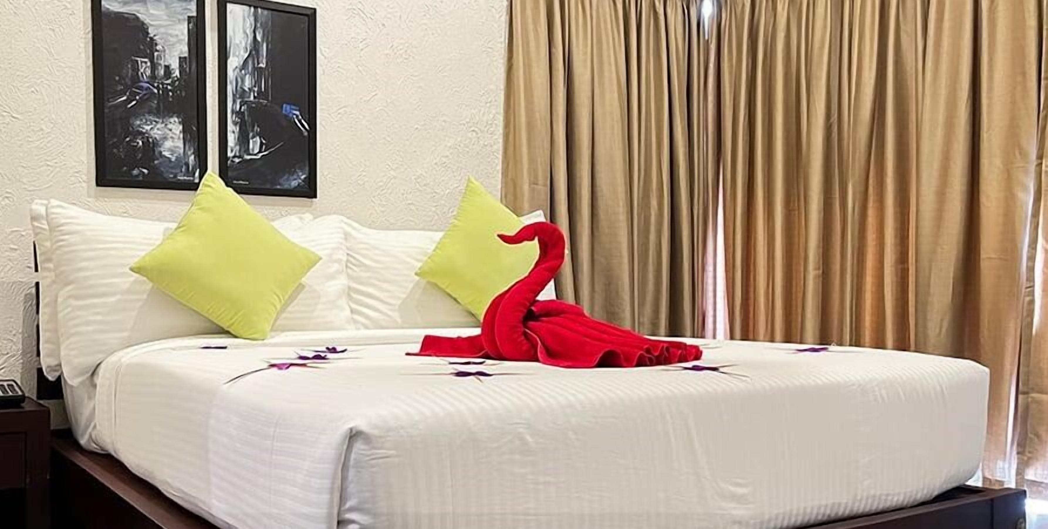 Una cama bien hecha con ropa blanca, dos almohadas y una toalla roja con forma de cisne.