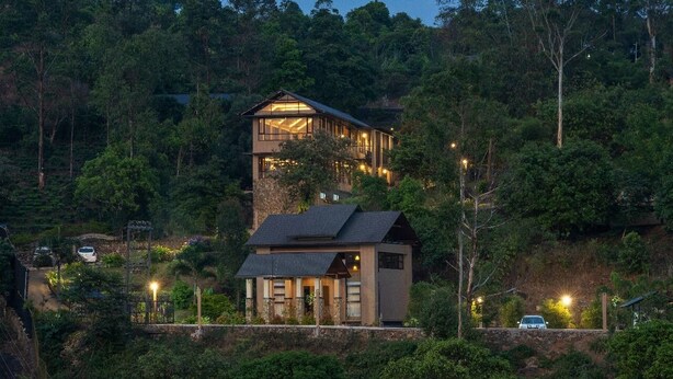 Una casa de dos pisos con un balcón grande, rodeada de bosque denso.