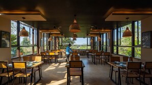 Un comedor amplio con ventanas grandes, varias mesas y lámparas colgantes.