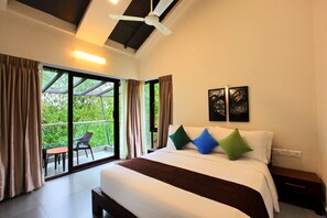A bedroom with a large bed, a ceiling fan, a nightstand, and a view of greenery through the window. - Tea Terrain Resorts & Spa (Peermade)