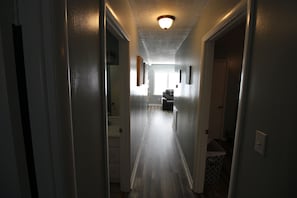Un pasillo estrecho con una lámpara en el techo, que conduce a una habitación con ventana y una silla.